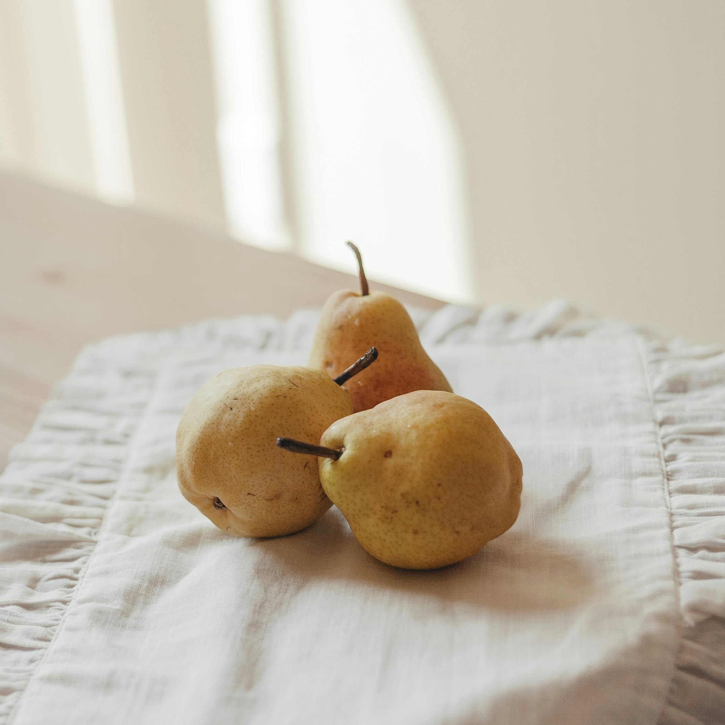Three ripe pears placed on a cloth under warm sunlight indoors.